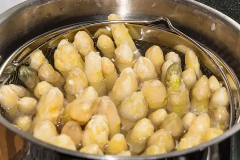 Spargel im Spargeltopf kochen. Die weißen Stangen garen in siedendem Wasser, bereit für ein köstliches Gericht.