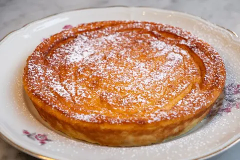 Migliaccio napoletano ricetta della nonna, dorato e cosparso di zucchero a velo, su un piatto decorato.