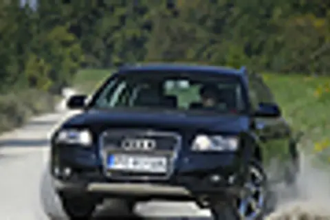 Ciemny Audi allroad pokonuje piaszczystą drogę, wzbijając kurz.