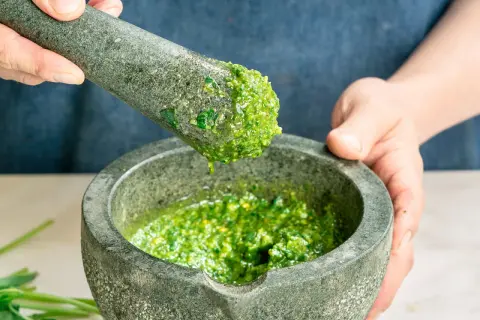 Frische Kräuter werden im Mörser zerstoßen, um ein leuchtend grünes Pesto zuzubereiten. Perfekt für einfache Pesto Rezepte.