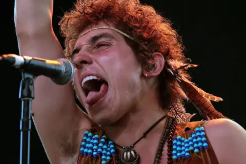 Josh Kiszka z Greta Van Fleet, jeden z członków zespołu, śpiewa z pasją do mikrofonu, ozdobiony piórami i koralikami.