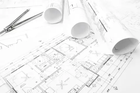 Plany budynków, gdzie szukać inspiracji i rozwiązań architektonicznych. Rysunki techniczne, cyrkiel i rolki z projektami.
