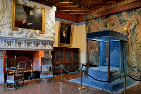 Intérieur du château de Chenonceau : cheminée monumentale, portraits, lit à baldaquin bleu et tapisseries somptueuses.