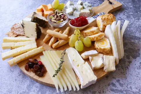 Una deliciosa presentación tabla de quesos con variedad de quesos, uvas, frutos secos y panecillos.