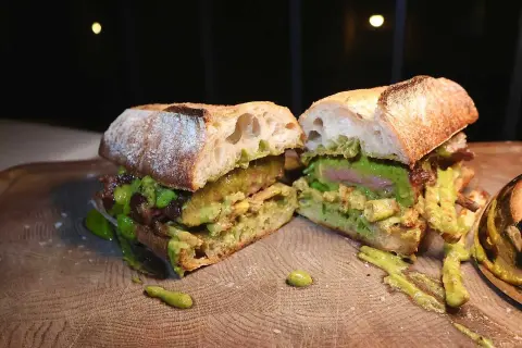 En saftig steak sandwich med avokado och en grön sås, upplagd på en träskärbräda.