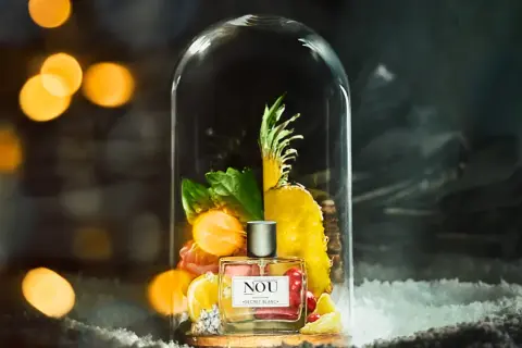 Perfumy NOU "Secret Blanc" w szklanej kopule, otoczone owocami i zielenią. Idealne miejsce, gdzie trzymać perfumy, by zachować ich świeżość.