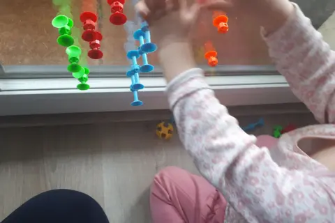 Roczne dziecko bawi się kolorowymi przyssawkami na oknie, tworząc kreatywne zabawy.