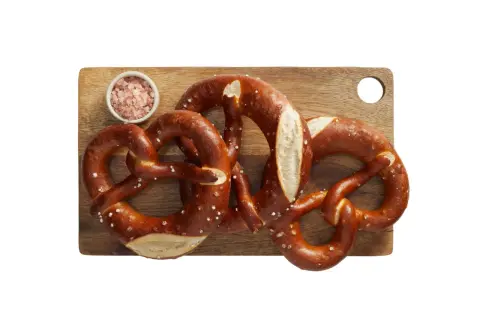 Trzy apetyczne precle z solą na desce, idealne na przekąskę. Zastanawiasz się nad precel Lidl kcal?
