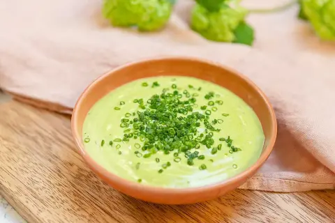Grön, krämig salsa verde toppad med finhackad gräslök i en skål på en träskärbräda.