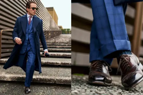 Uomo con outfit old money: completo blu a quadri, cappotto lungo, cravatta e scarpe stringate marroni.