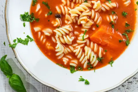 Zupa pomidorowa z makaronem fusilli i kawałkami marchewki. Aby jak zmniejszyć kwasowość zupy, dodaj szczyptę sody.