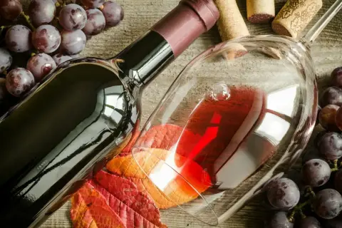 Uva Sangiovese, vitigno del Brunello di Montalcino, accompagna una bottiglia e un calice di vino rosso, su un tavolo di legno rustico.