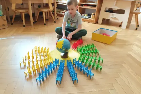 Chłopiec bawi się klockami w kształcie krzesełek, tworząc okręgi wokół globusa. To nauka przez zabawę w stylu metoda montessori.