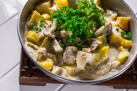 Pyszna potrawka z kurczaka ze śmietaną, grzybami i ziemniakami, udekorowana świeżą natką pietruszki.