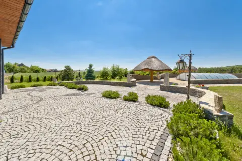 Piękny ogród z krętymi ścieżkami wyłożonymi kostką granitową, altaną krytą strzechą i basenem pod kopułą.