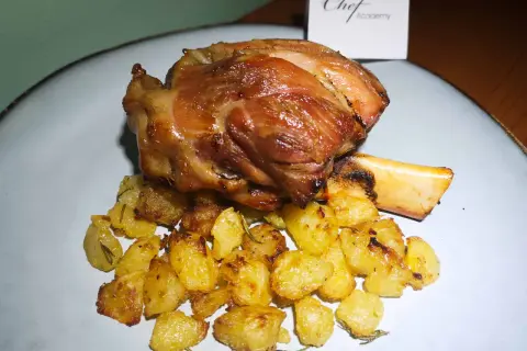 Stinco di maiale succulento e dorato, servito con patate arrosto croccanti e profumate al rosmarino.