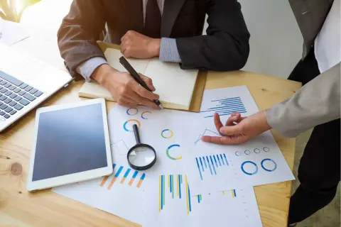 Deux personnes analysent des graphiques et des données pour un audit énergétique. Un ordinateur portable et une tablette sont sur la table.