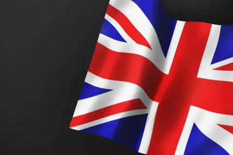 Flaga Wielkiej Brytanii, symbol nadziei na pozwolenie na pracę w UK dla Polaków. Czerwono-biało-niebieskie pasy falują na ciemnym tle.