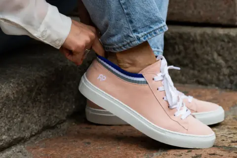 Mani che sistemano calzini a righe dentro scarpe rosa cipria, un dettaglio per il riempimento scarpe grandi.