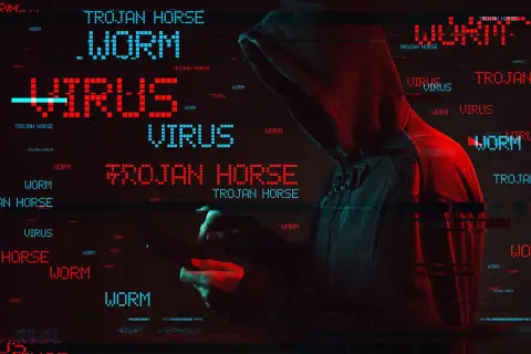 Haker w kapturze, otoczony przez migoczące napisy "WORM", "VIRUS" i "TROJAN HORSE". To pokazuje, co to trojan - złośliwe oprogramowanie udające coś pożytecznego.