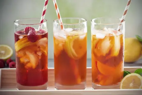 Trois verres de thé vert glacé, garnis de fruits rouges et de citron, prêts à être dégustés.