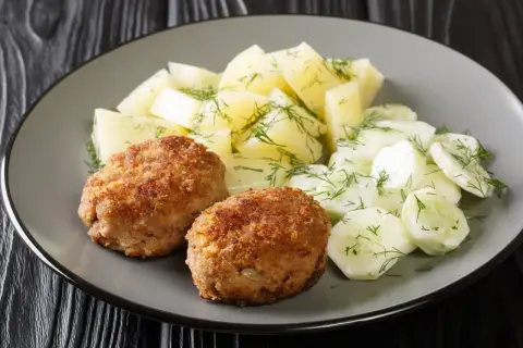 Dwa kotlety mielone z ziemniakami i mizerią na talerzu.