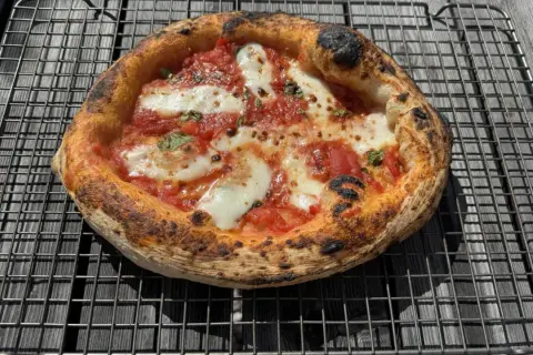 En perfekt napolitansk pizza med bubblig, bränd kant, tomatsås och smält mozzarella på ett galler.