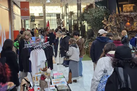 Gente comprando en un rastro de Zaragoza. Hay ropa colgada en percheros y puestos con libros y adornos.