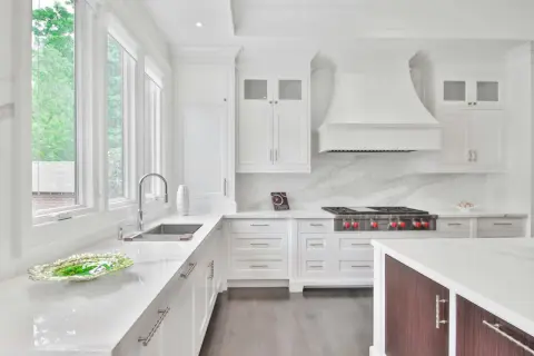 Cocina moderna blanca con encimeras de cuarzo. Muebles de cocina de melamina con tiradores plateados. Campana extractora y estufa profesional.