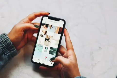 Dłonie trzymające telefon, na ekranie widoczny profil Instagrama z moimi pracami. Niestety, moje urządzenie iPhone niedostępne.
