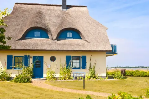 Charmantes Haus mit Reetdach und blauen Akzenten. Ein Blick auf die Frage: was kostet ein reetdach?