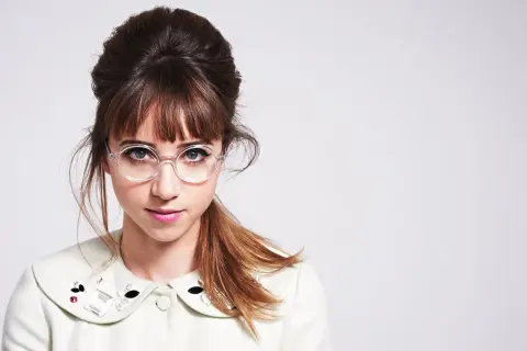 Ein junges Mädchen mit einem Dutt und Pony, das eine runde Brille trägt. Ihre Frisur mit Brille ist ein echter Hingucker.