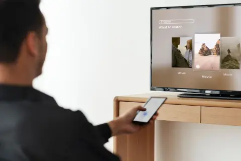 Mężczyzna steruje telefonem, by dowiedzieć się, jak udostępnić internet z telefonu na telewizor i oglądać filmy.