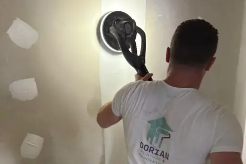 Un artisan utilise une ponceuse girafe pour lisser un mur en placo. C'est la ponceuse idéale pour un travail de finition impeccable.