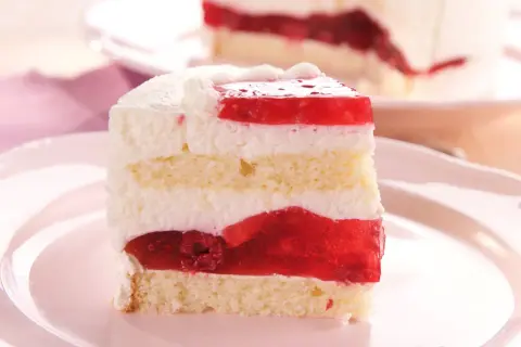 Ein saftiges Stück Frau Holle Kuchen mit Biskuit, Sahne und roter Fruchtfüllung, verziert mit Himbeeren.