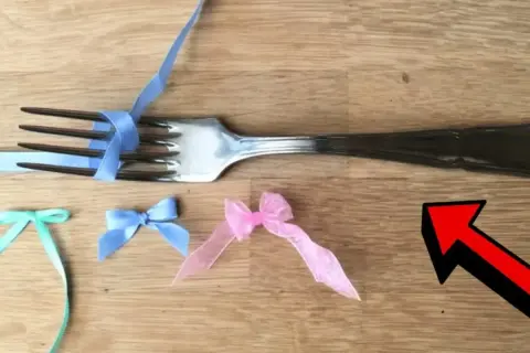 En gaffel används för att knyta rosett med blått band. Små rosetter i mintgrönt, ljusblått och rosa ligger på träbordet.