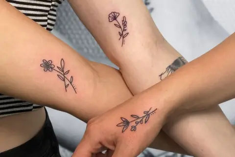 Drei Arme zeigen zarte, elegante Tattoos von Blumen und Zweigen.