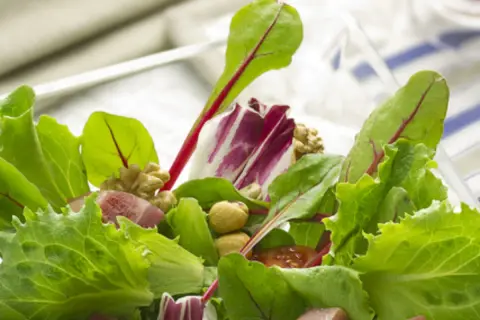 Ensalada fresca con brotes tiernos, nueces y trozos de jamón.