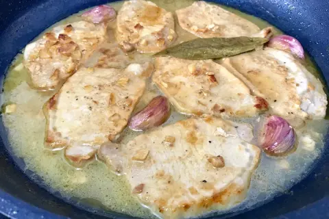 Filetes de lomo al ajillo dorándose en una sartén con ajo y laurel.