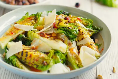 Deliciosa ensalada de cogollos a la parrilla, cubierta con lascas de queso parmesano y un aderezo vibrante.