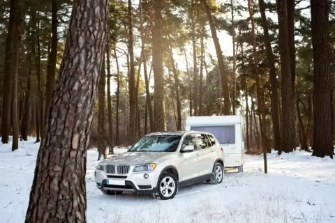 Biały SUV z przyczepą kempingową w zimowym lesie. Idealne warunki do podróży z prawem jazdy B+E.