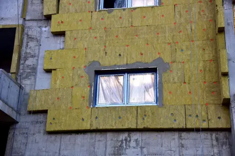 Pannelli isolanti gialli applicati al muro grezzo di un edificio in costruzione, creando un cappotto casa per l'isolamento termico.