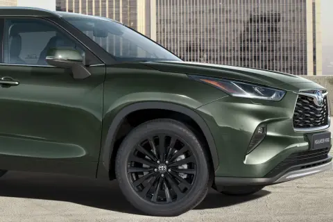 Zielony Toyota Highlander z czarnymi felgami stoi przed nowoczesnym budynkiem.