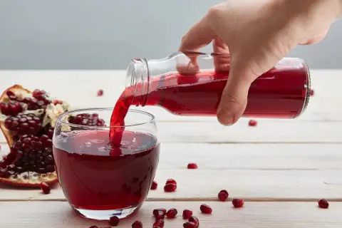 Ręka nalewa sok z granatu do szklanki. Obok leży połówka owocu. Ile pić dziennie?