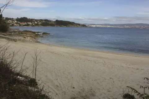 Arena dorada en la playa temperans, con el mar azul y una ciudad al fondo.