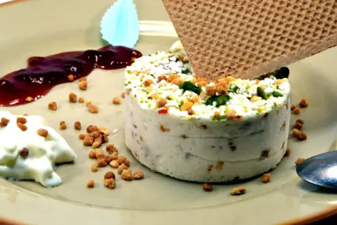 Un délicieux nougat glacé, parsemé de fruits secs et de pistaches, servi avec un coulis de fruits rouges et une touche de crème.