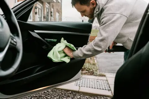 Man rengör bilens dörrpanel med en grön trasa. En fräsch doft i bilens interiör är målet.