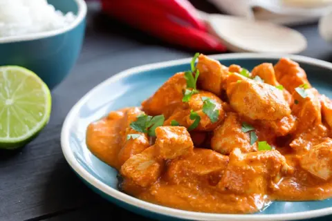 Un saporito spezzatino di pollo in salsa cremosa, guarnito con prezzemolo fresco, accompagnato da riso bianco e spicchio di lime.
