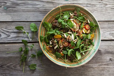 En härlig quinoa sallad med körsbärstomater, gröna blad och mandelspån, serverad i en vacker skål på en träbakgrund.