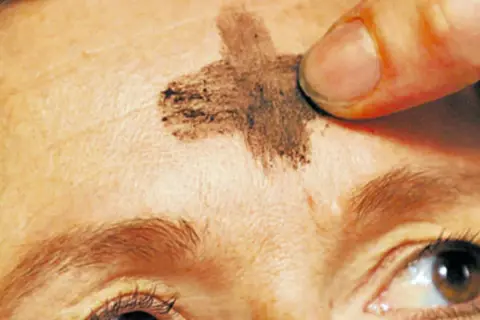 Ein Finger zeichnet ein Aschekreuz auf die Stirn. Dies ist ein Symbol für Aschermittwoch und den Beginn der Fastenzeit.